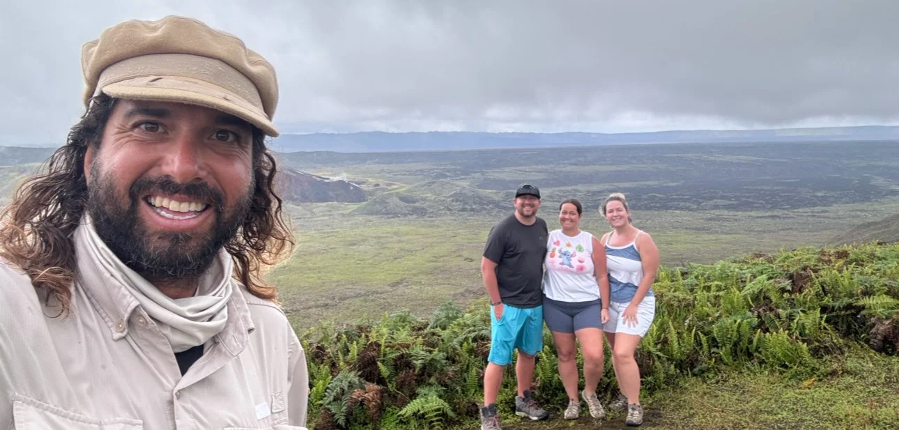 Three people and a guide on the Sierra Negra hike in the Galápagos Islands, standing in a lush green area with volcanic landscape in the background.
