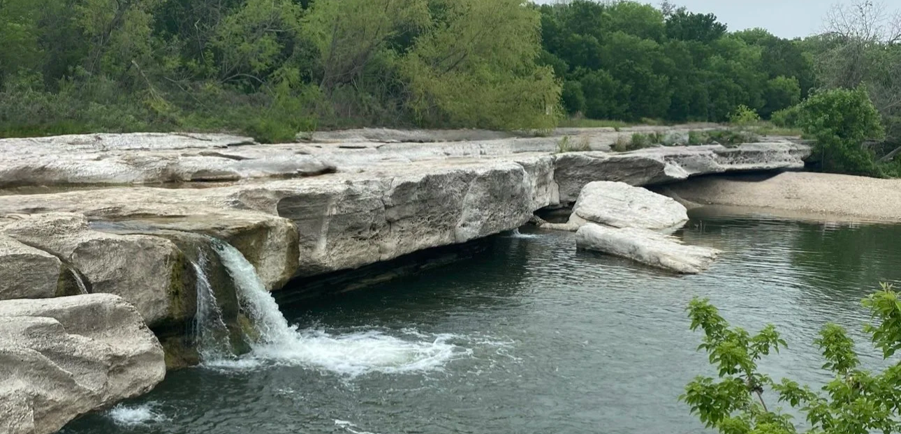 Waterfalls cascading over rocky ledges at McKinney Falls State Park, Texas, surrounded by lush greenery.