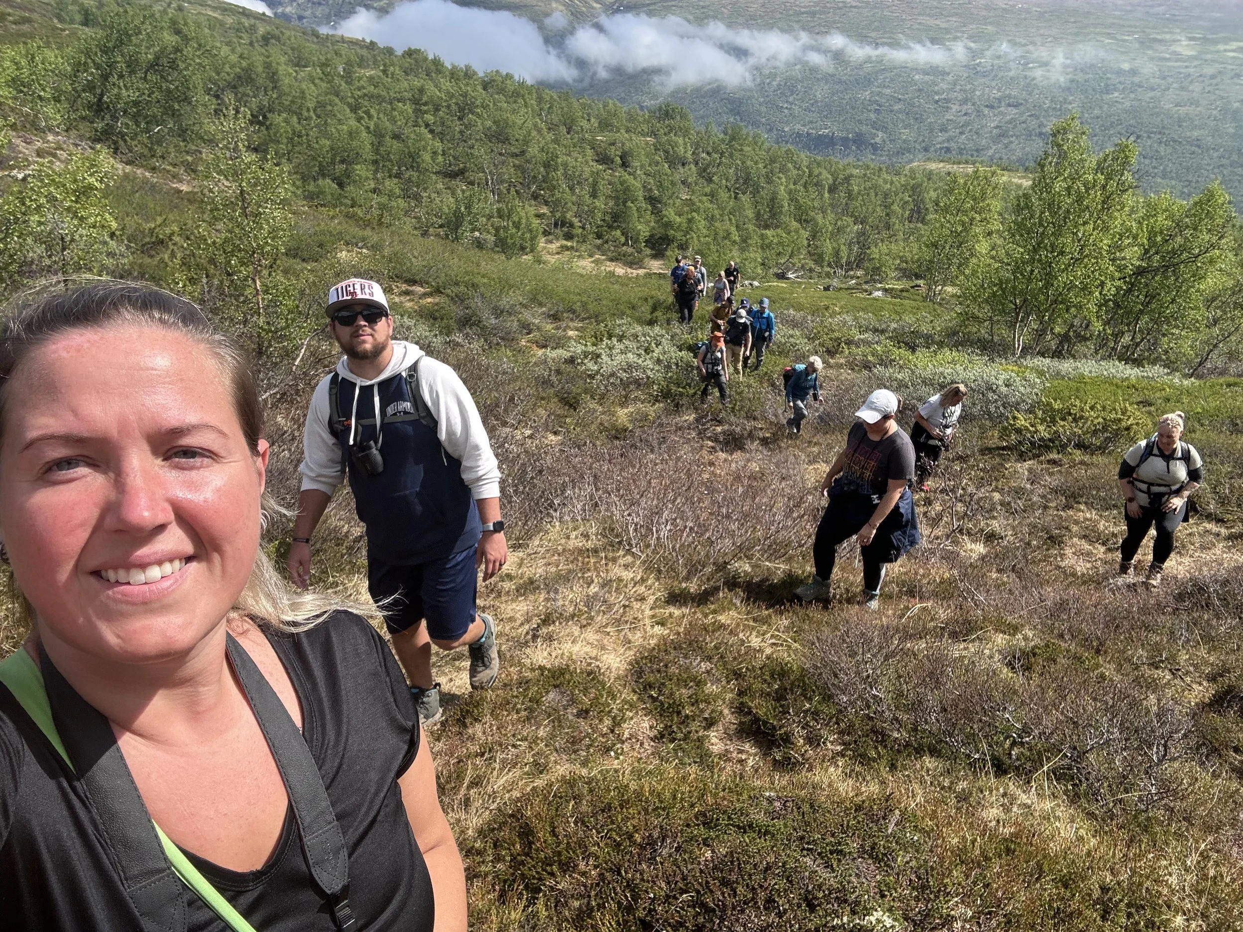 Woman smiling and taking a selfie with a group of people participating in a musk ox walking safari hike in Dombås, Norway, Arctic landscape in the background