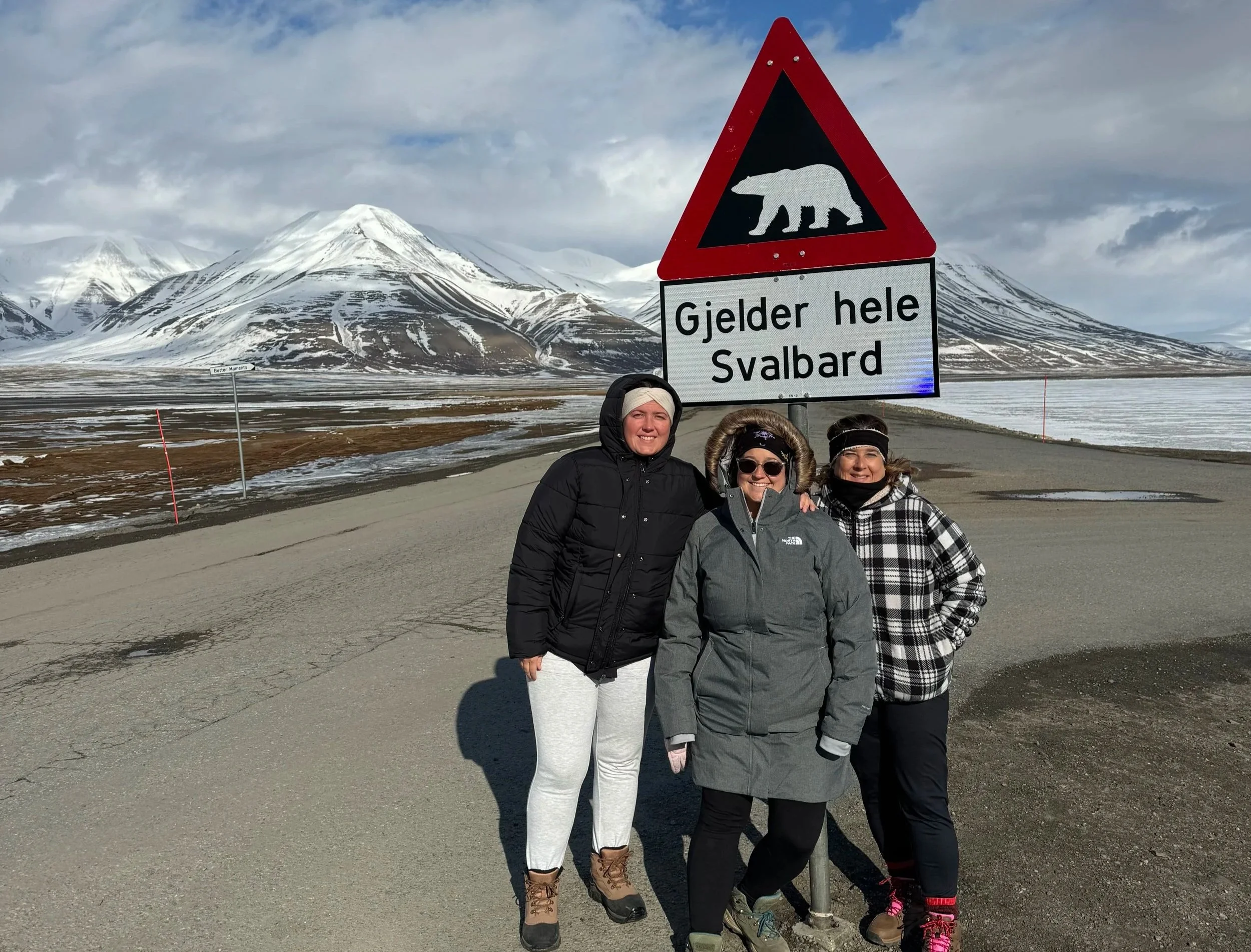 Three women standing in front of a polar bear warning sign in Svalbard, Arctic safety sign with tundra landscape in the background