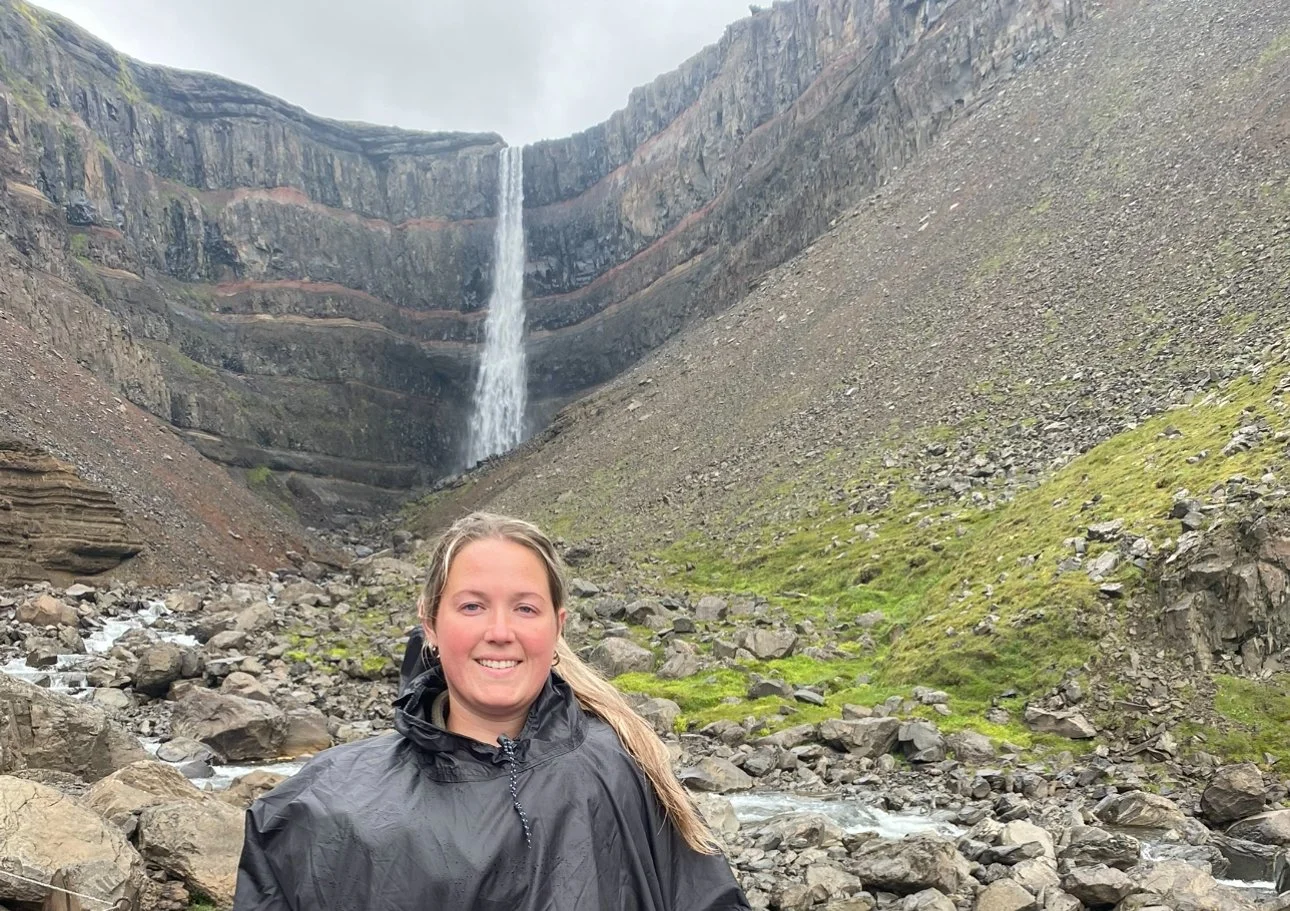 Person smiling in front of Hengifoss waterfall in Iceland.