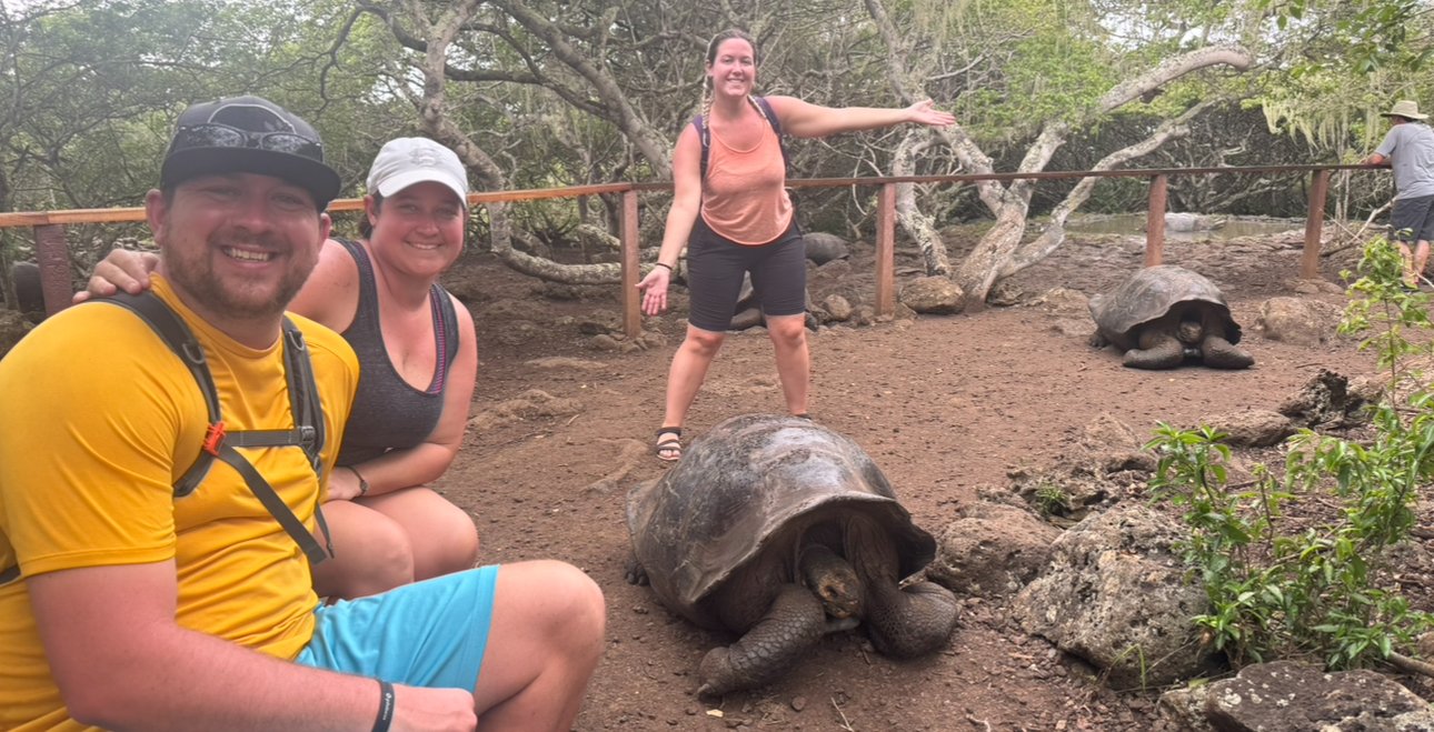 Three people posing with giant tortoises in the Galápagos Islands.