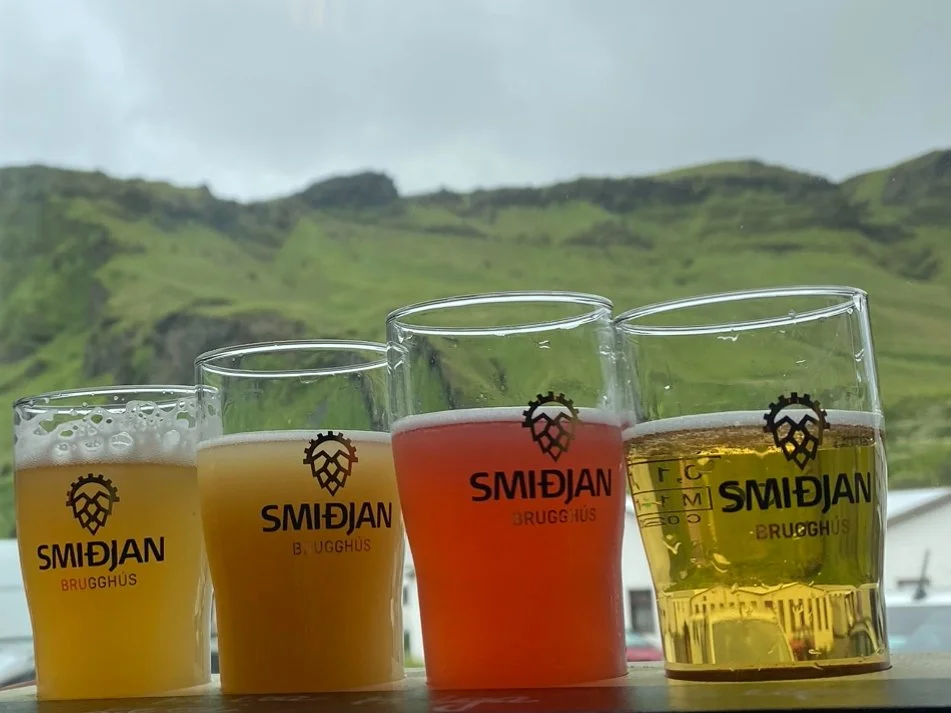 A flight of beers on a table at Smiðjan Brugghús Brewery with a green scenic view visible through the window.