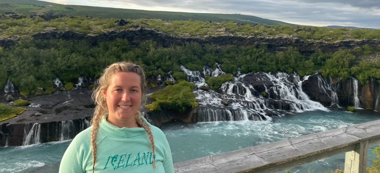 Woman smiling in front of the Hraunfossar and Barnafoss waterfalls in Iceland.