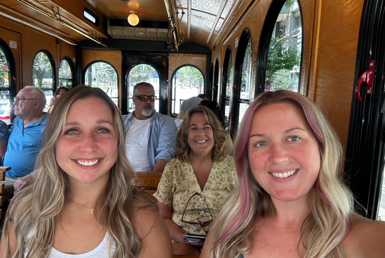 Three women smiling and enjoying an Atlanta trolley tour with the trolley in the background.