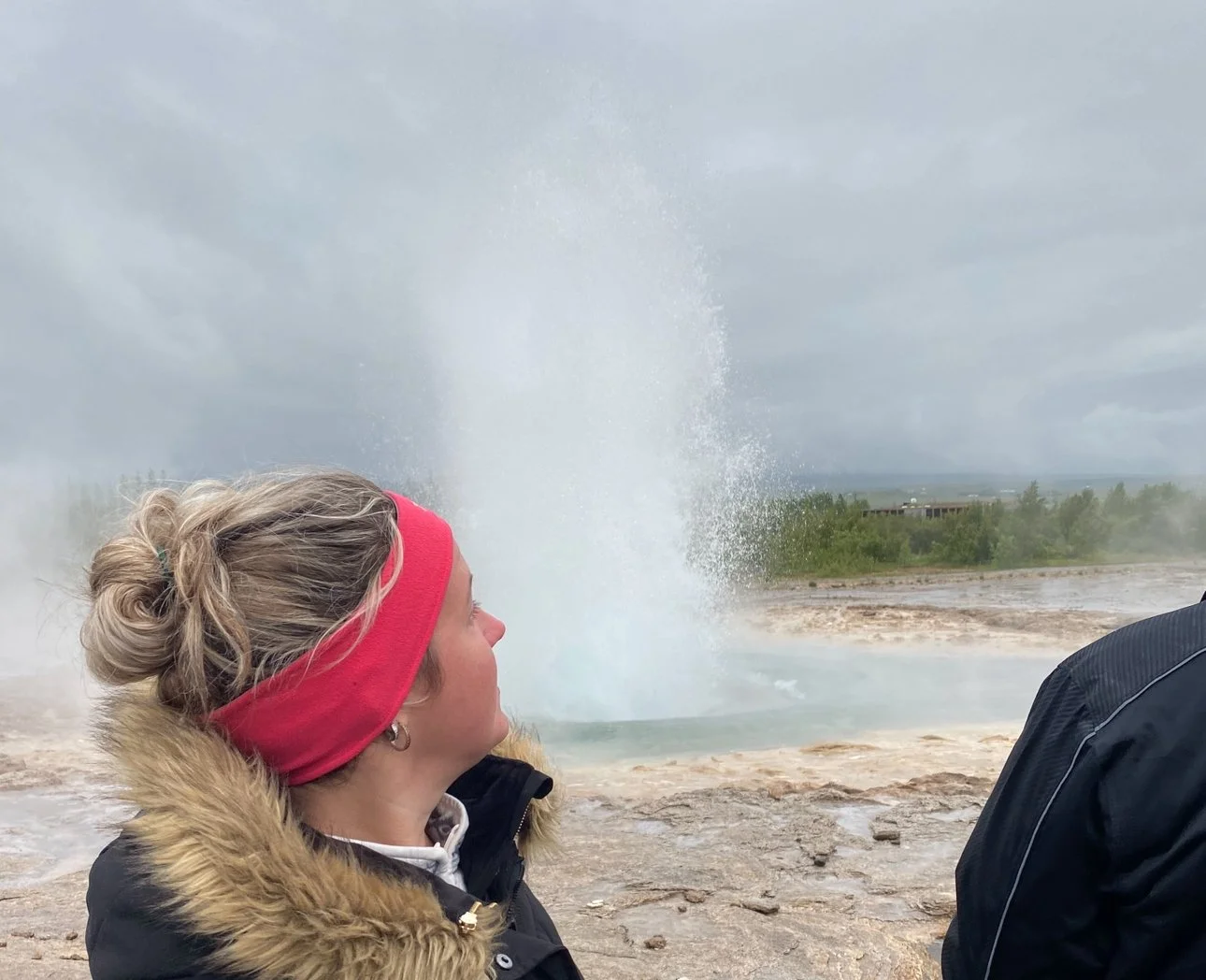 Person standing and watching the Strokkur Geyser erupt in Iceland.