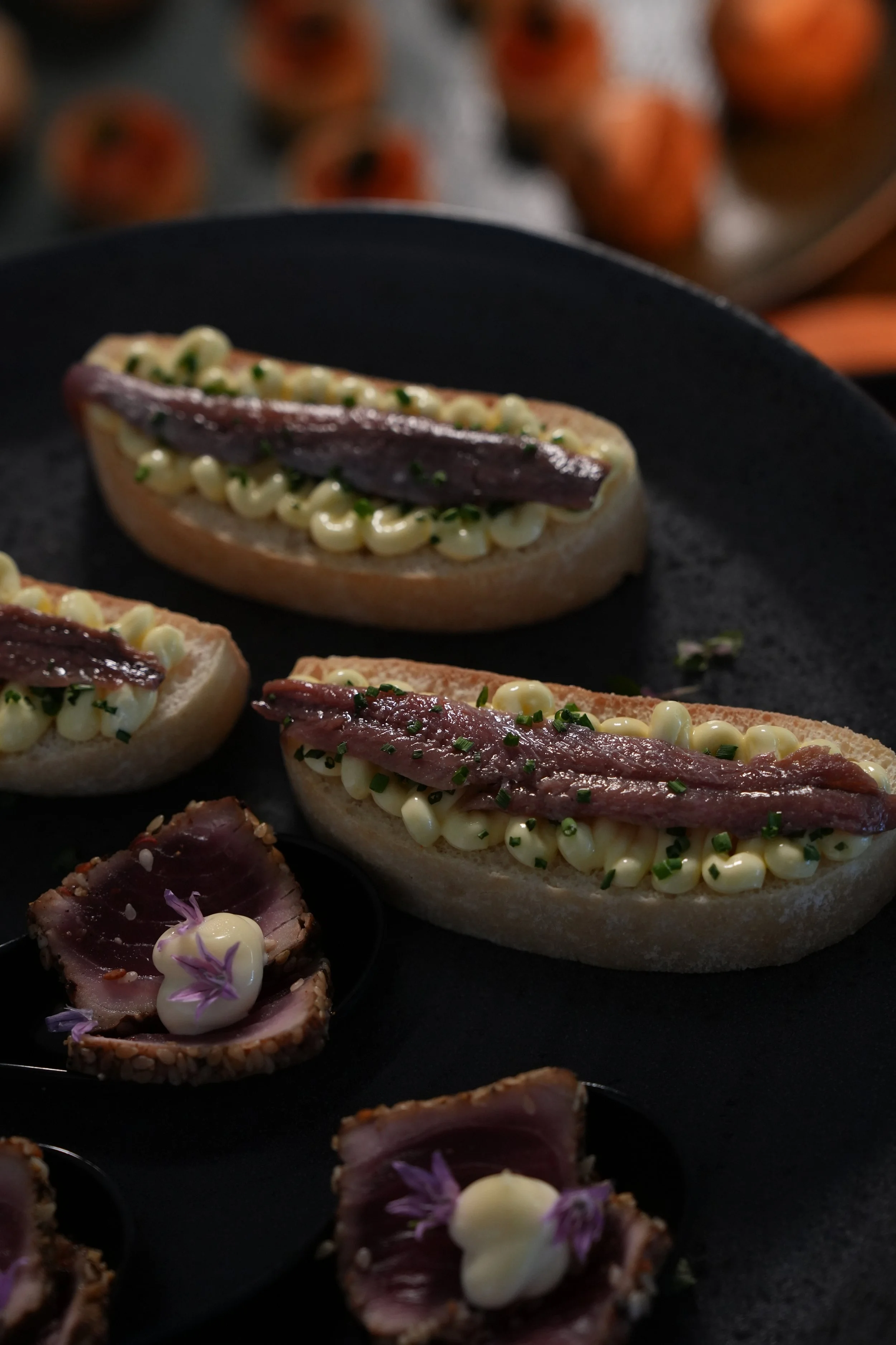 Appetizer with baguette slices topped with mayonnaise, herbs, and slices of seared tuna, garnished with edible flowers.