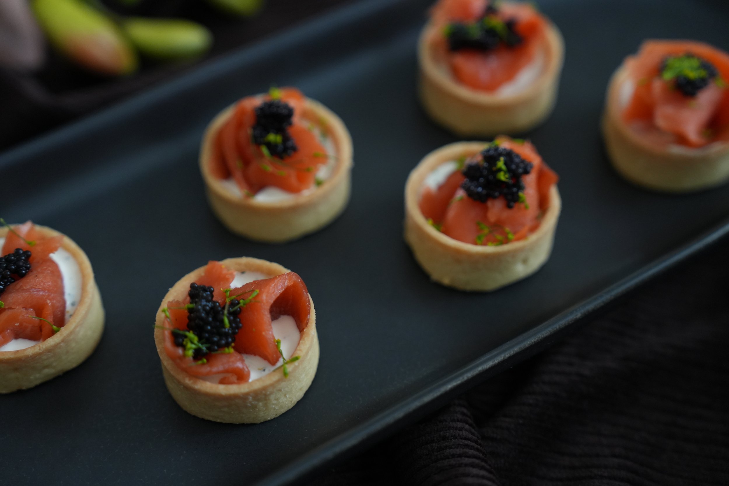 Tray of small appetizer tartlets with slices of smoked salmon, black caviar, and green garnish. Catering Sydney