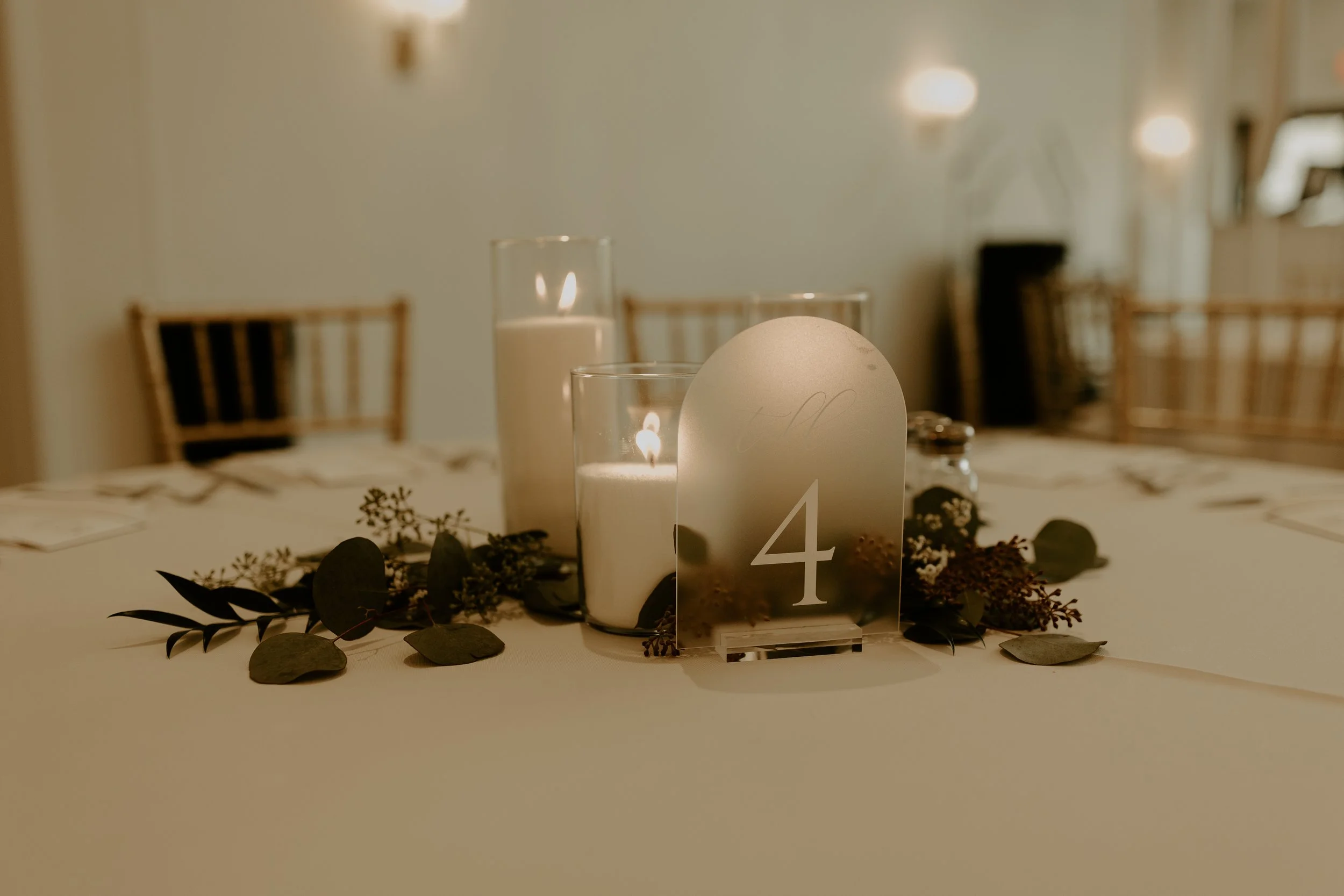 Table centerpiece with candles, greenery, and a table number four sign at an event venue.