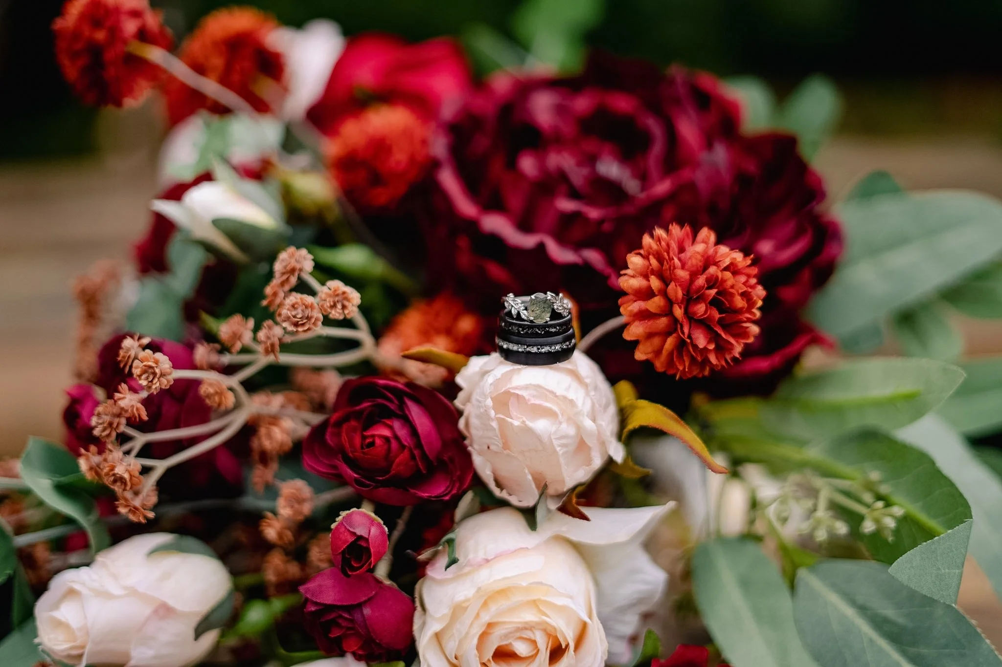 Close-up of a bouquet with red, white, and pink flowers and green leaves, with three rings placed on a white flower in the center.