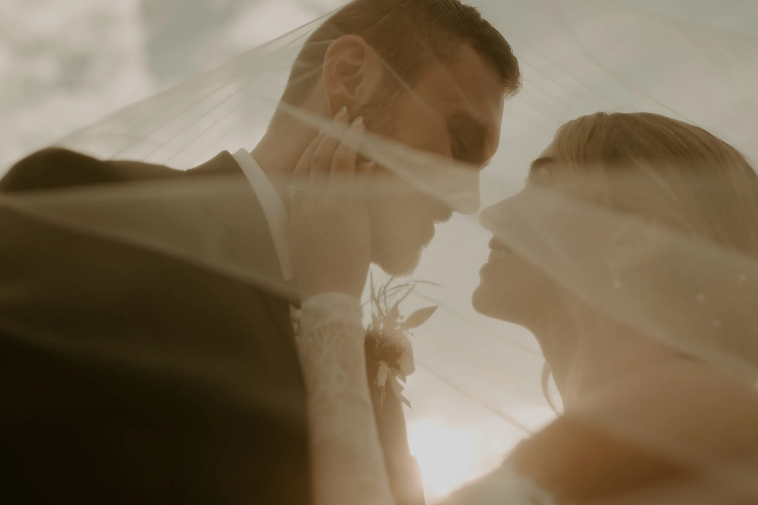 A close-up romantic moment between a bride and groom, smiling and touching foreheads, with a bridal veil and natural light.