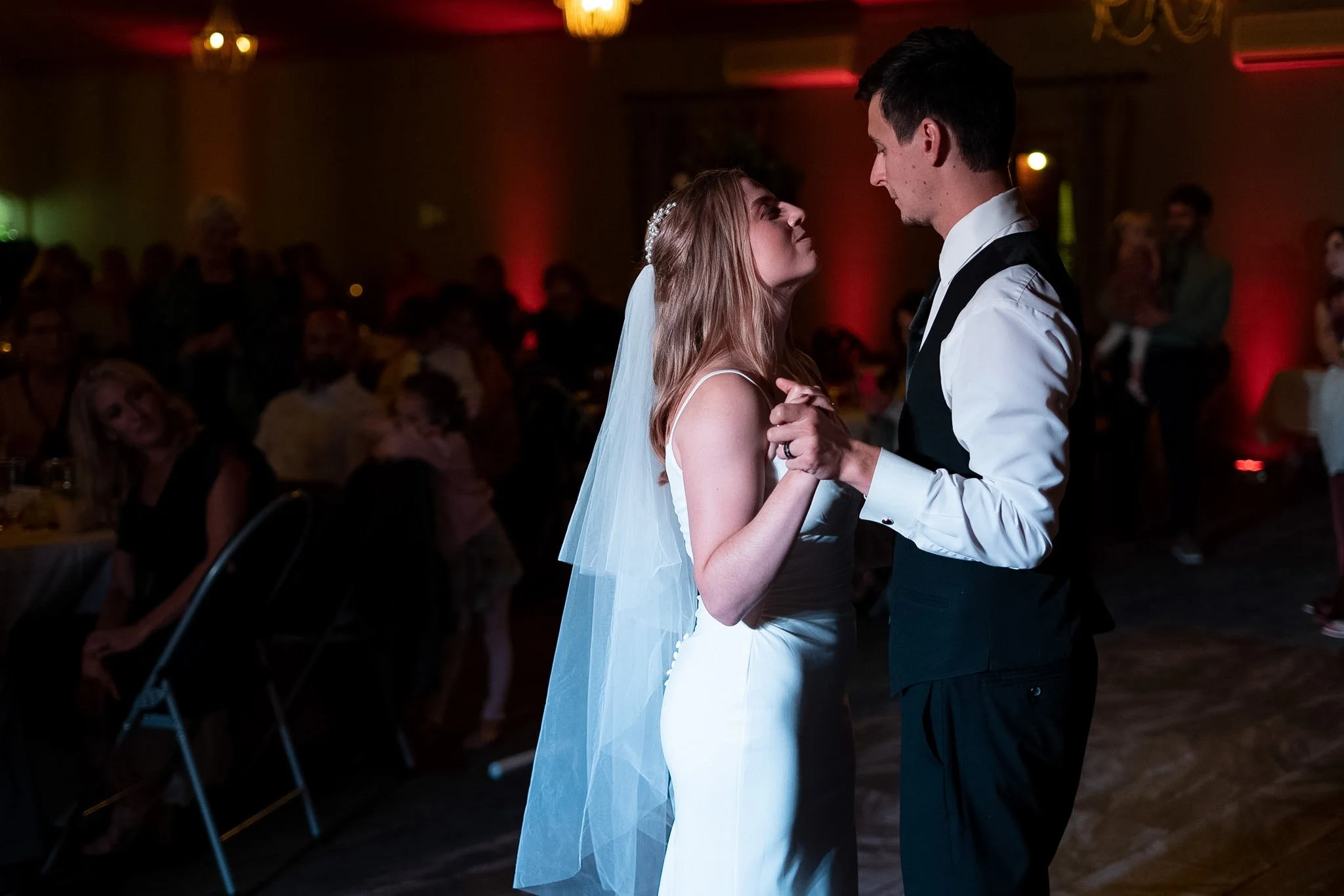 A bride and groom are dancing closely at their wedding reception, holding hands and gazing into each other's eyes.