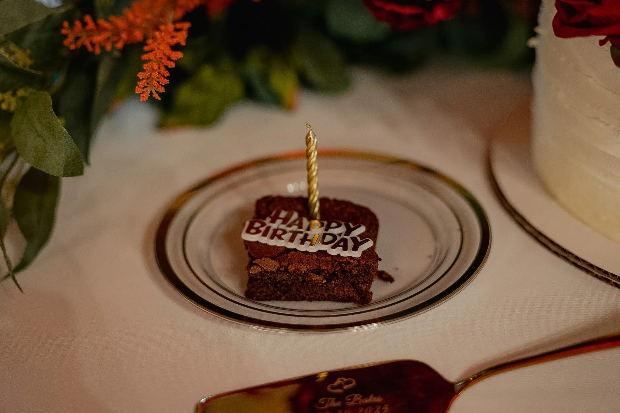 A small piece of chocolate cake with a birthday candle and a 'Happy Birthday' decoration on top, placed on a white plate.