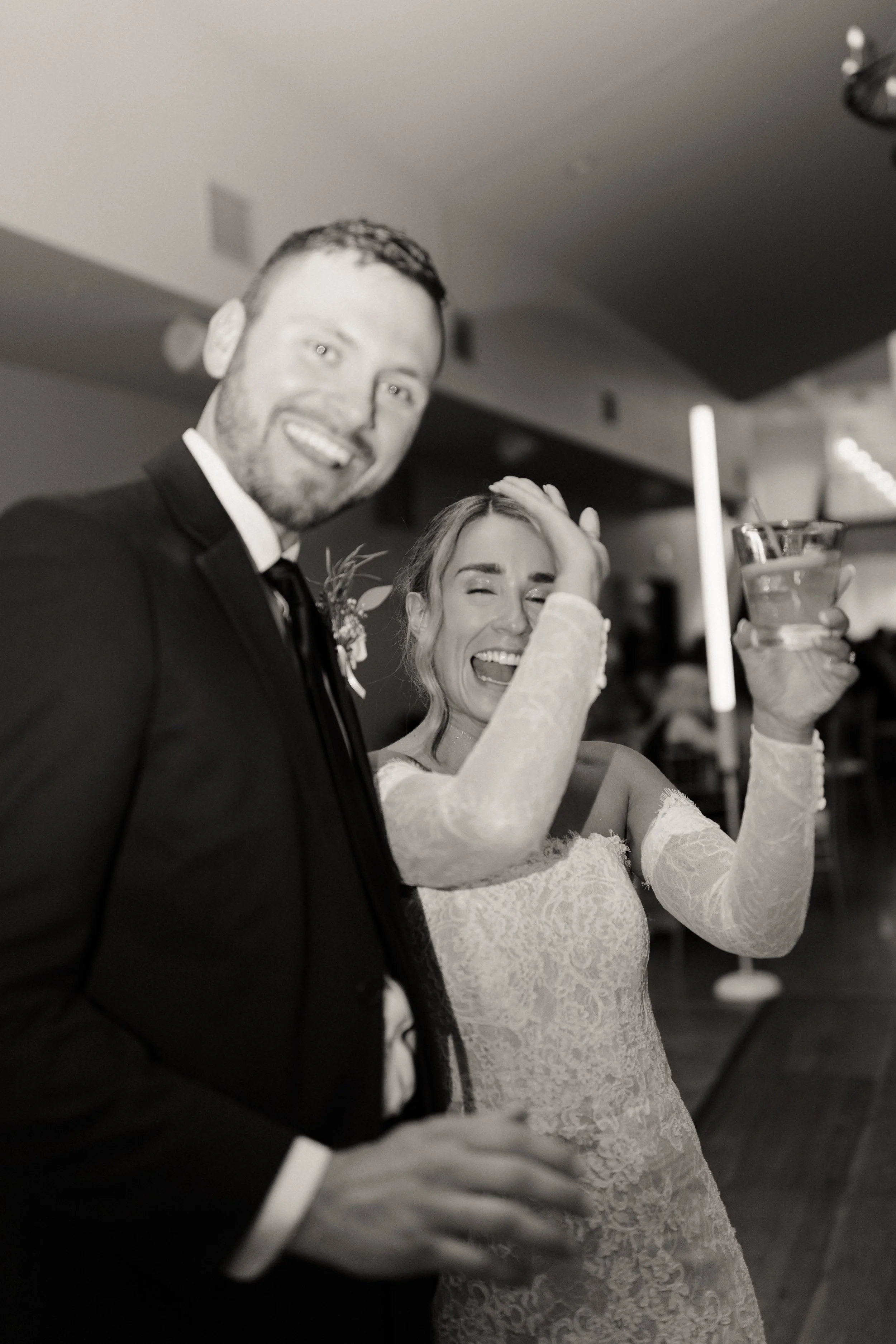 A man and woman celebrating, both holding drinks and smiling, at a wedding reception.