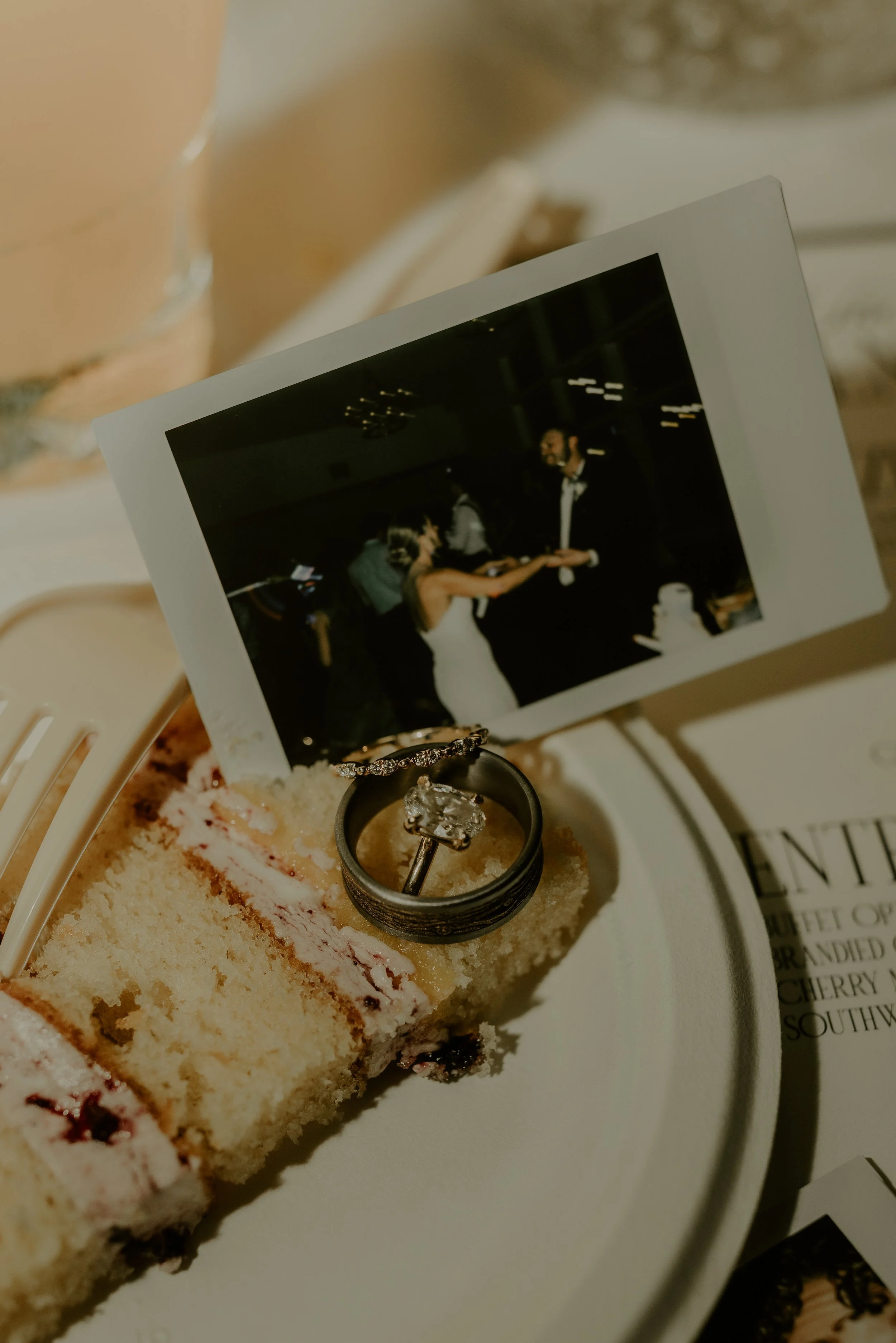 Wedding cake slice with a photograph of a couple dancing, and two rings placed on top of the cake.