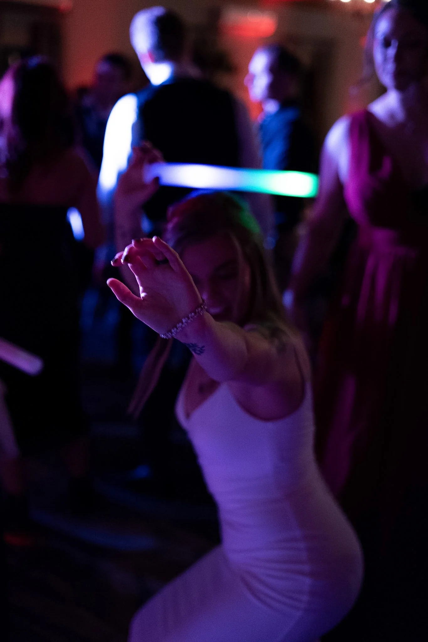 A woman in a pink dress dancing and pointing towards the camera at a party or dance event, with others dancing and socializing in the background.