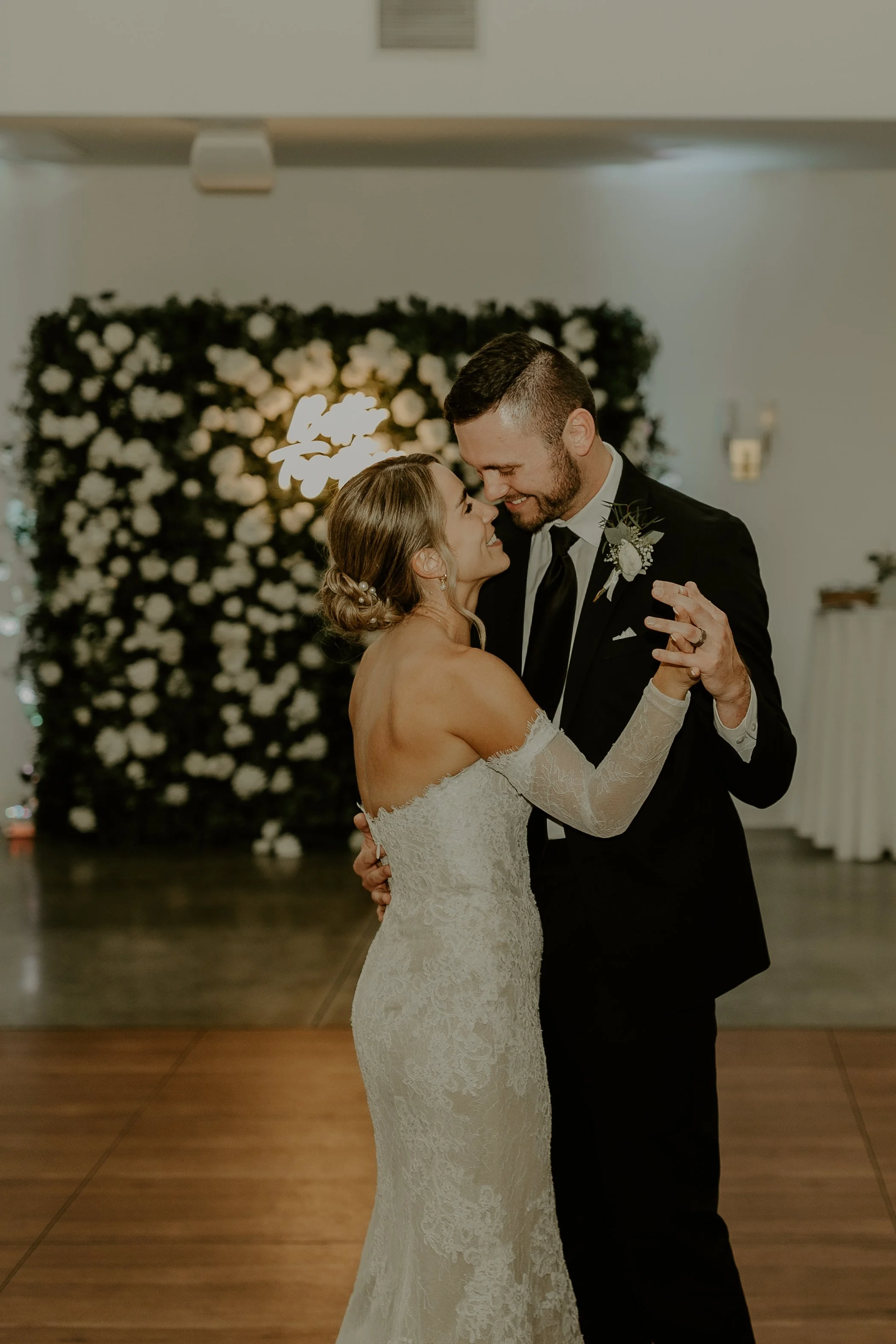 A bride and groom dance closely together at their wedding reception, smiling and sharing an intimate moment.