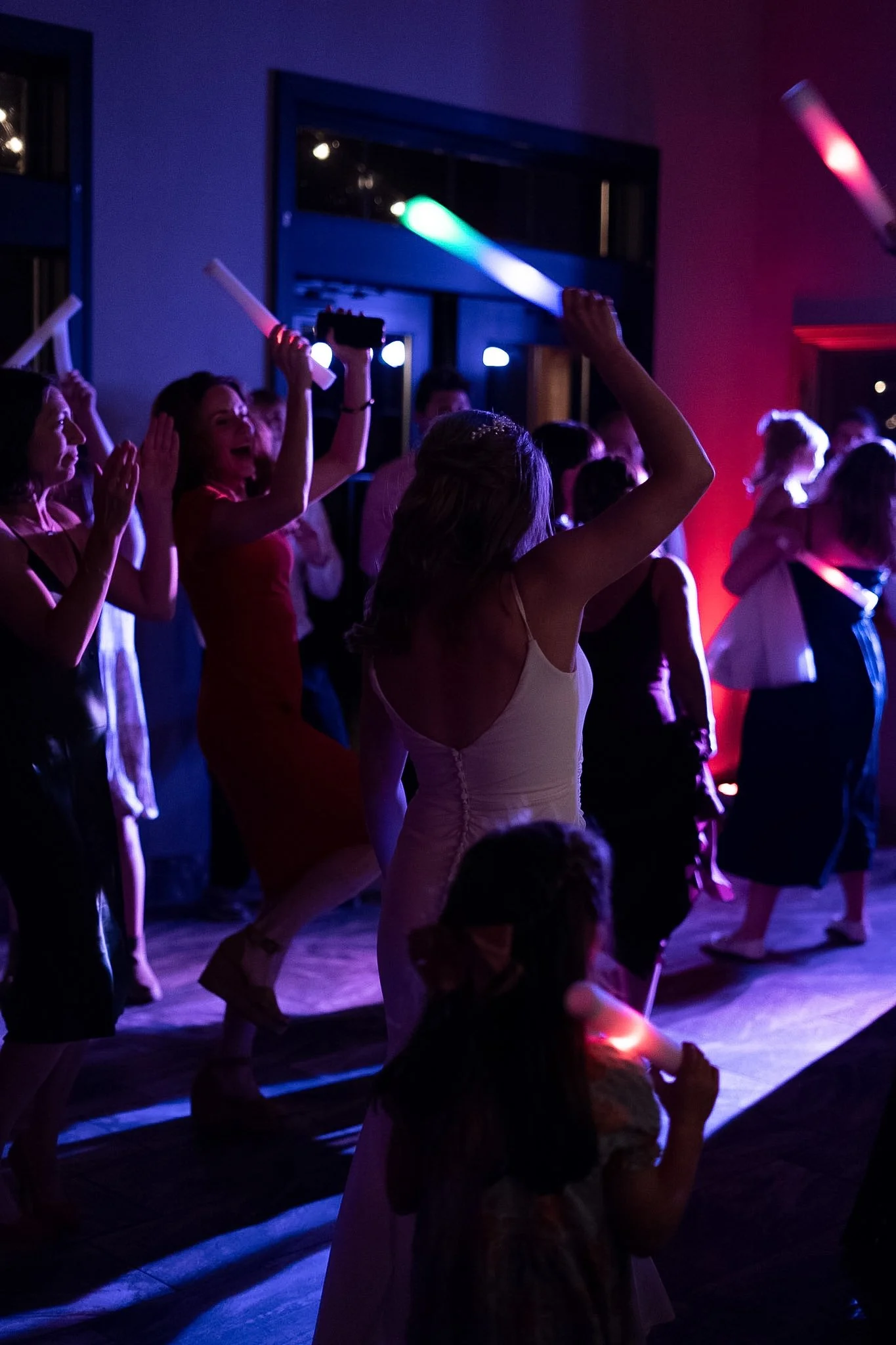 People dancing and celebrating at a party with colorful glow sticks and vibrant lighting.