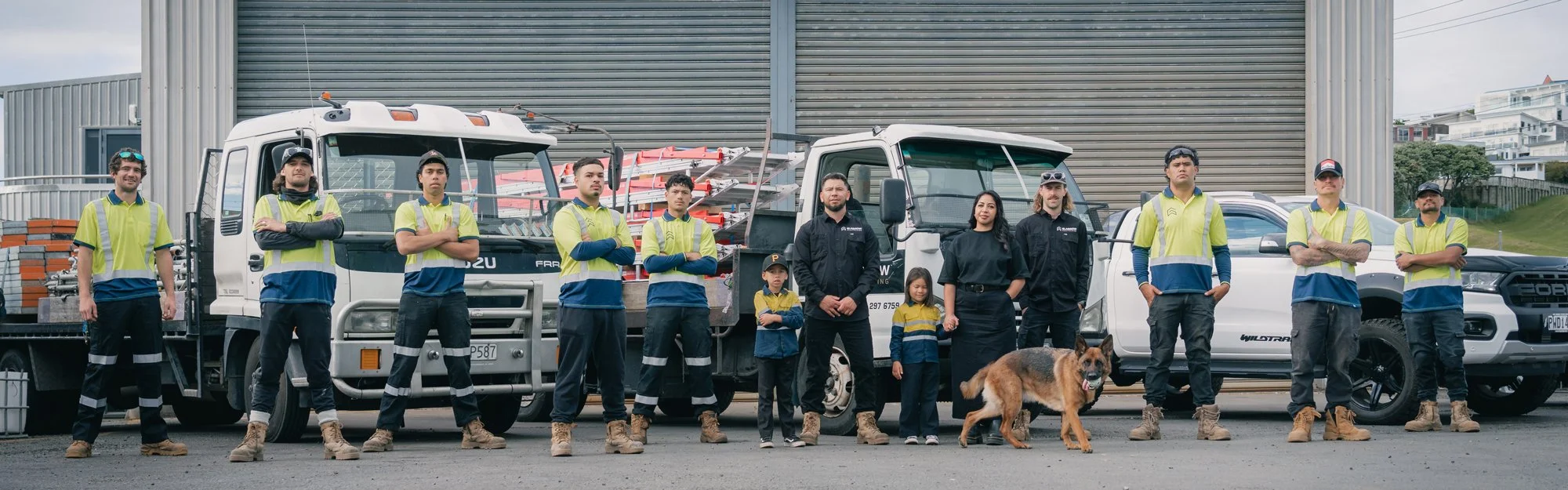 The full Glasgow Scaffolding team and their dog standing in front of service trucks, wearing safety vests and work boots.