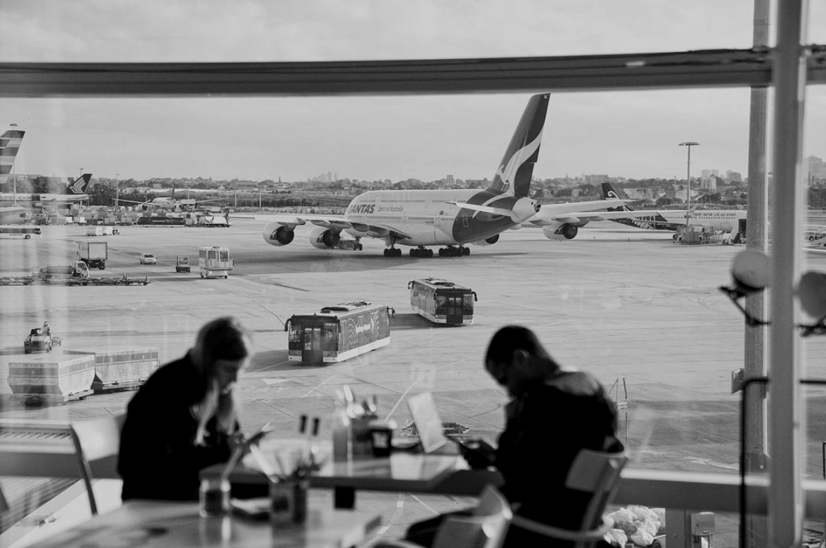 People sitting at a table near a large airport window, with a Qantas airplane on the tarmac outside.