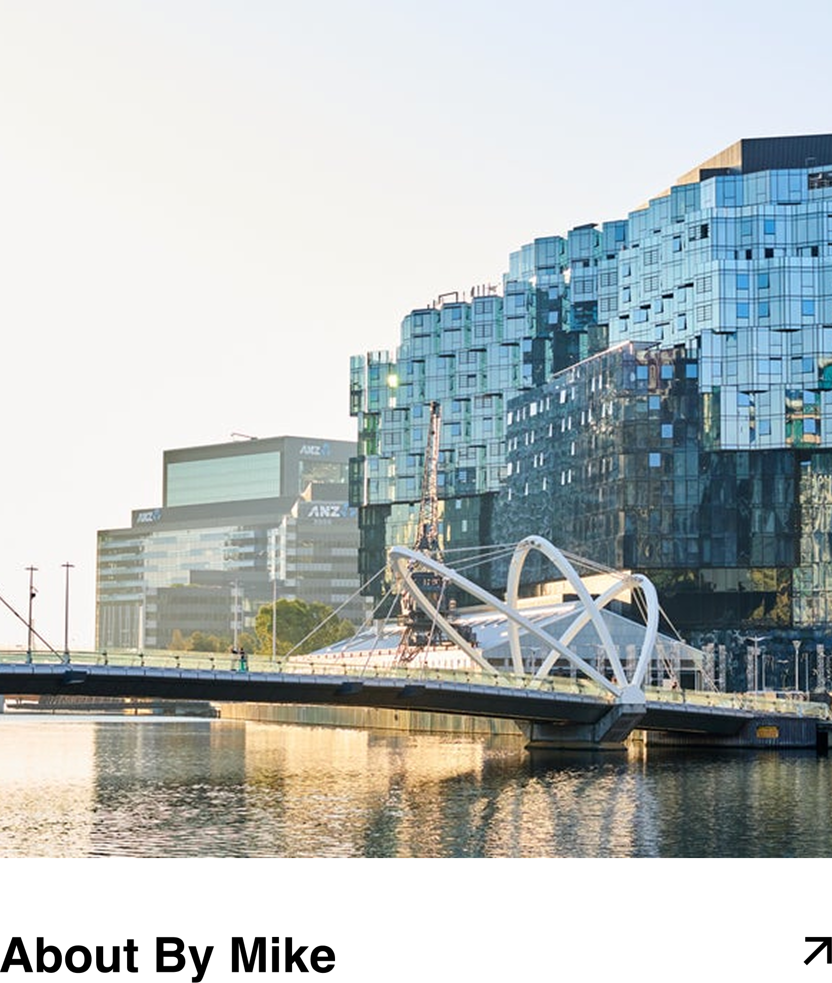 Modern glass building and a pedestrian bridge over water with reflections, in an urban setting