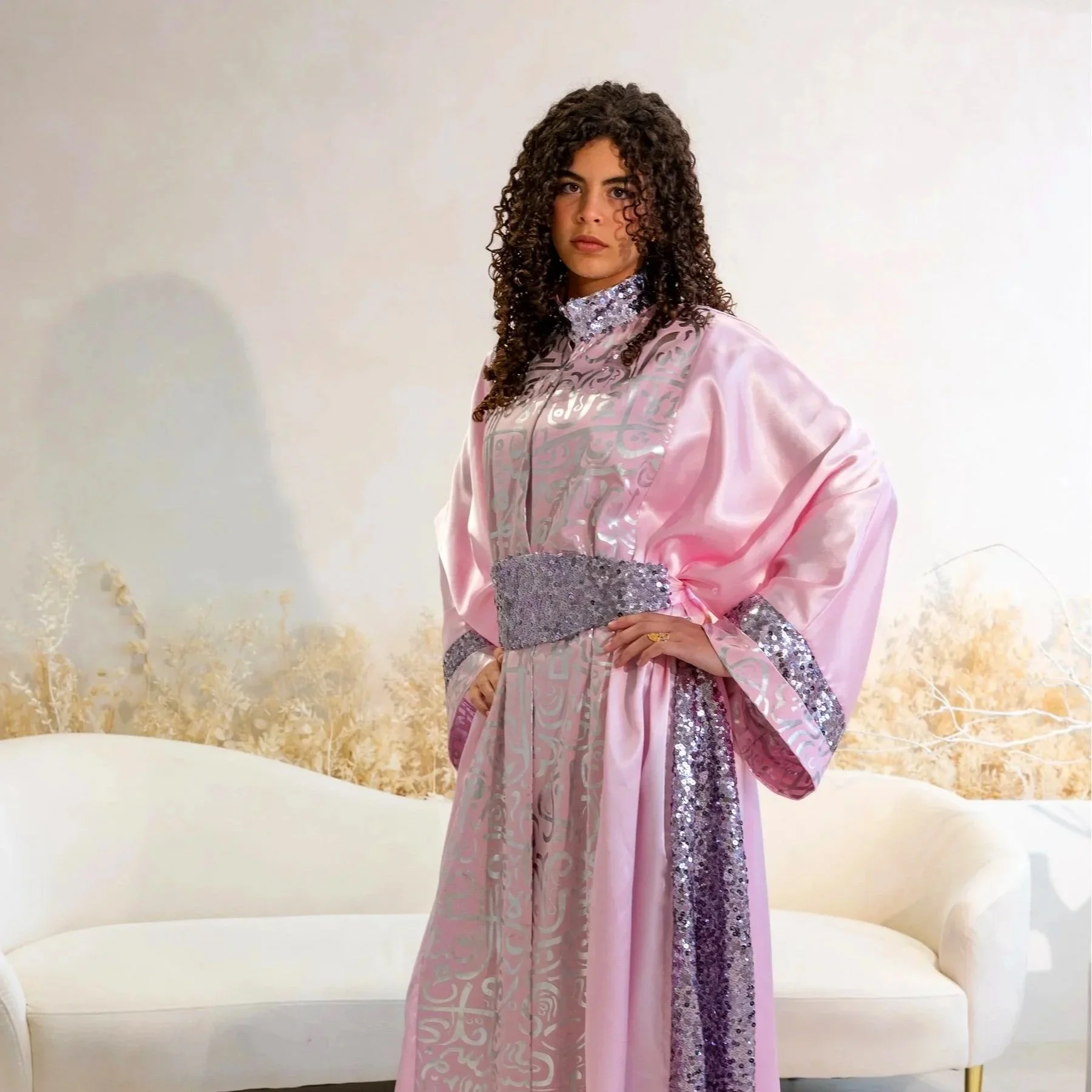 A young woman in a pink ceremonial gown with silver embellishments, standing in front of white marble stairs and columns.