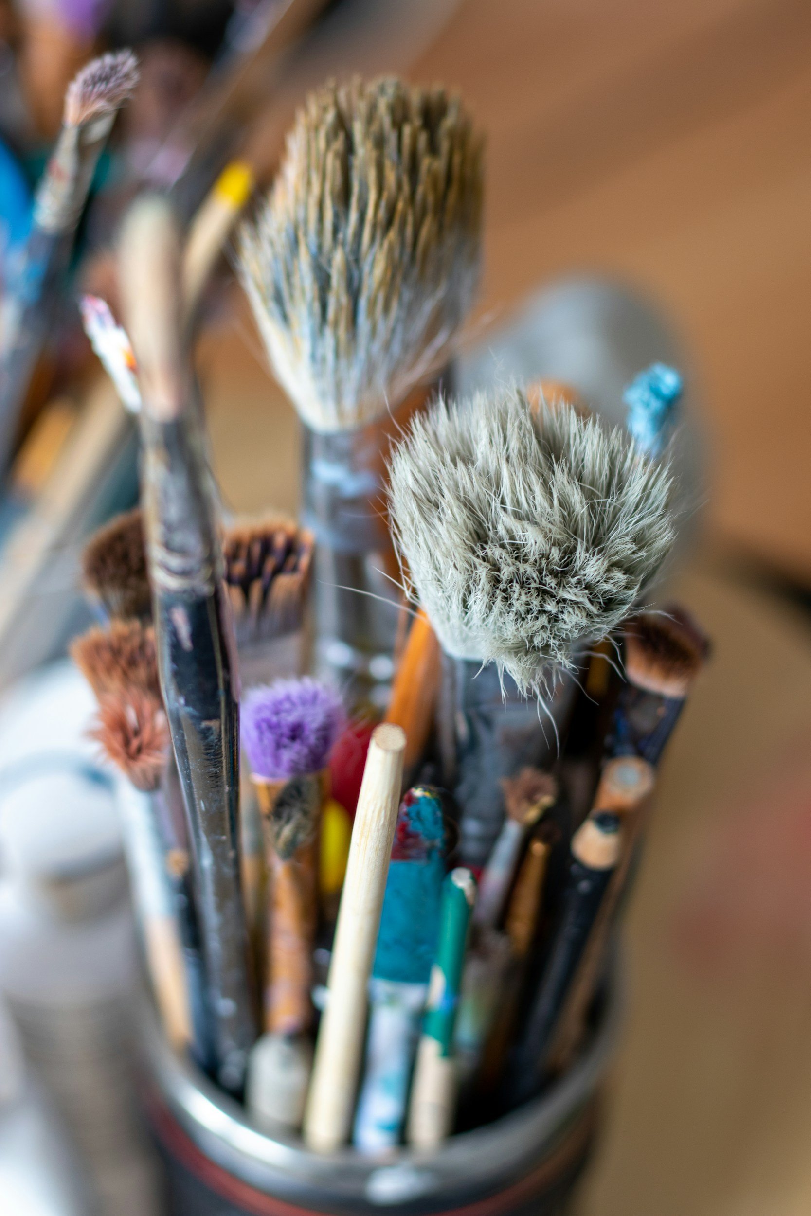 A collection of paintbrushes of various sizes and types stored in a container, with some brushes having colorful or textured bristles.