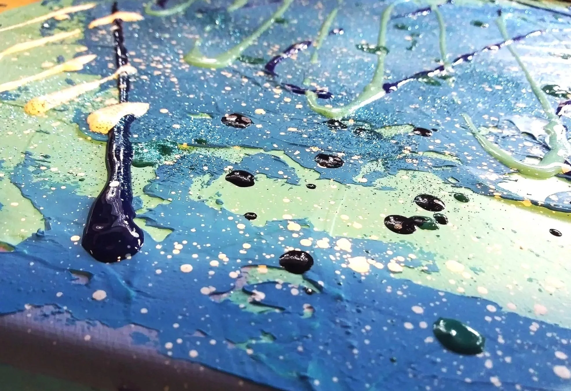 Close-up of a colorful abstract painting with splatters of black, white, yellow, and shades of blue and green paint.