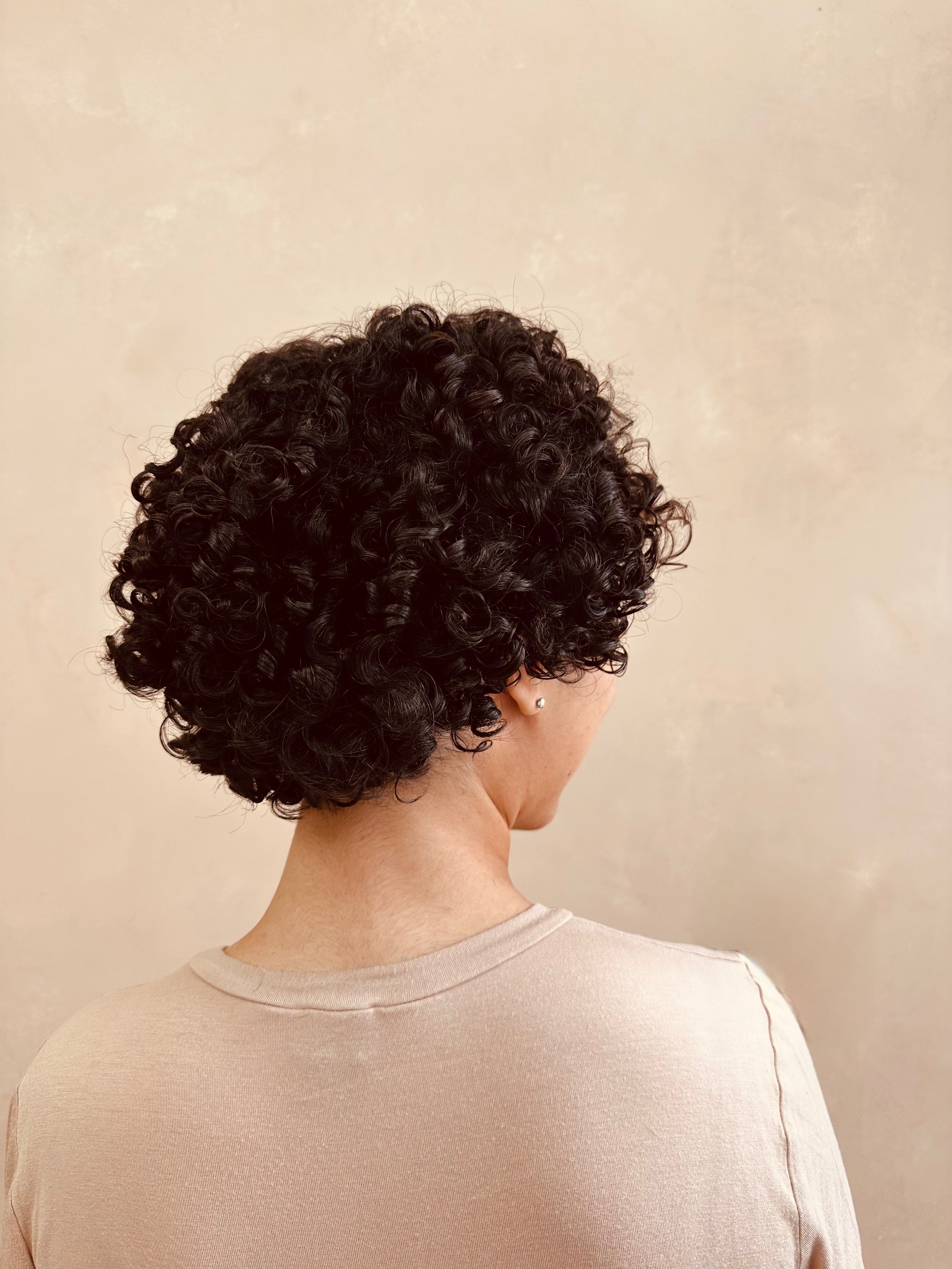woman with tightly curled hair, . roman clay wall. 3c curl pattern, type 4 hair , black hair, afro, haircut, textured hair, curly hair salon, black woman, melanin queen, 4a hair, 4b hair, 4c hair, 3b hair, curly, coily hair, kinky hair, wavy hair.