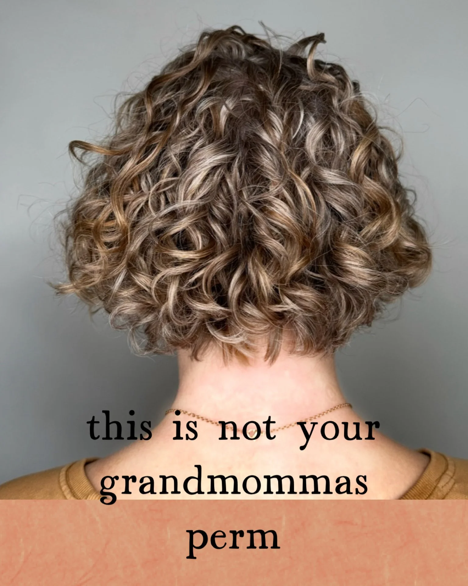 Back of a person with short, curly, blonde hair. Text on the image reads 'this is not your grandma's perm, permed hair vancouver, east vancouver salon, east village salon, modern perm