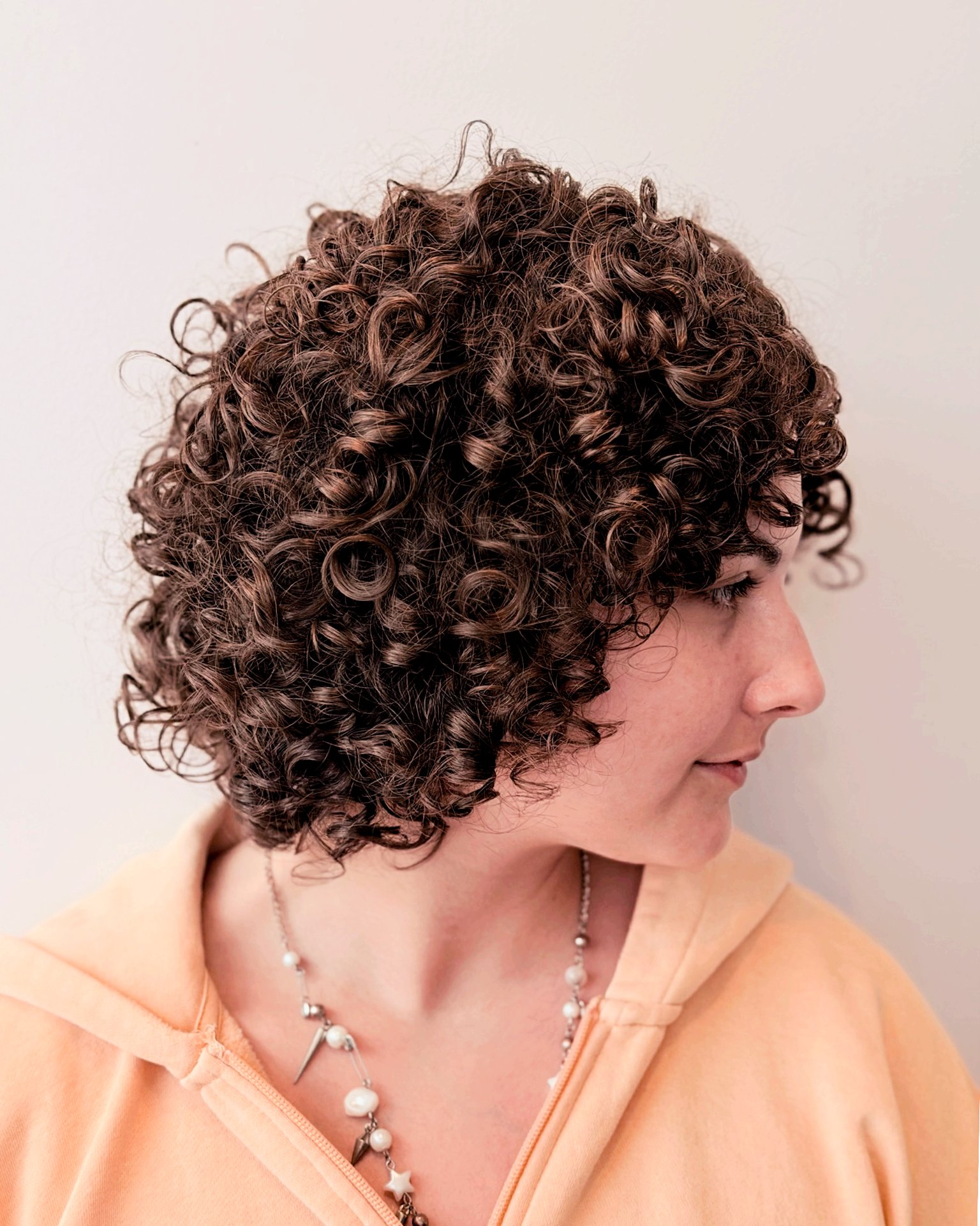 A woman with short, tight, dark curly hair, 4a hair, 4b hair, 4c hair, 3a hair, 3b hair,3c hair, curly hair, coily hair, kinky hair, wavy hair. round haircut, multicultural, ethnic salon