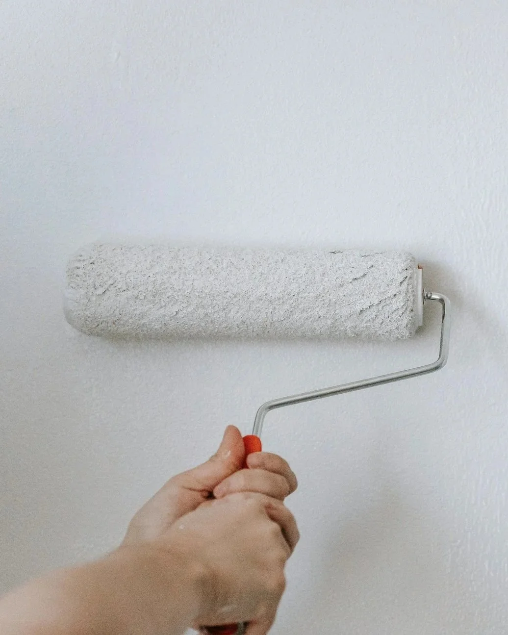 a hand rolling a paint roller, covered in white paint, against a wall