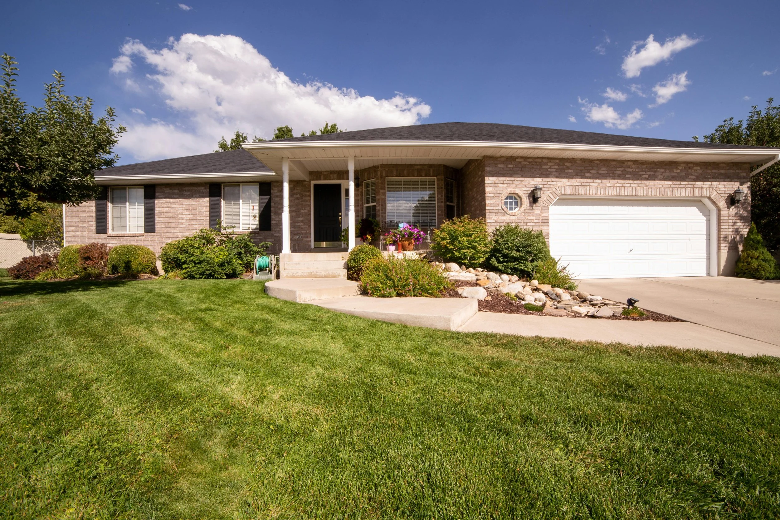 curbside view of a one-story house with a green lawn and a small but pretty garden, giving the house better curb appeal