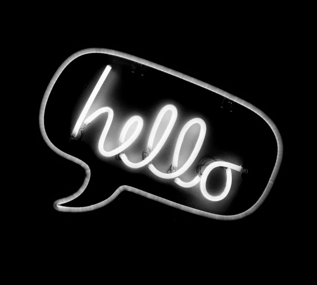Neon sign in the shape of a speech bubble with the word 'hello' written inside in cursive.