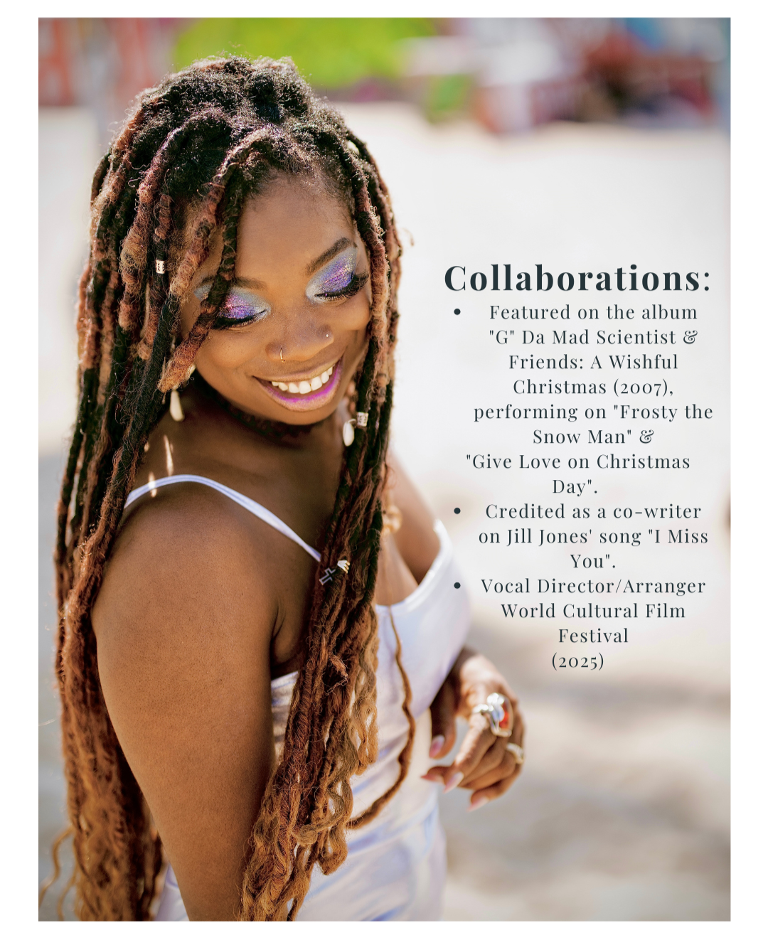 A woman with long, styled dreadlocks and colorful eye makeup smiling while looking down, wearing a white top and jewelry standing outdoors.