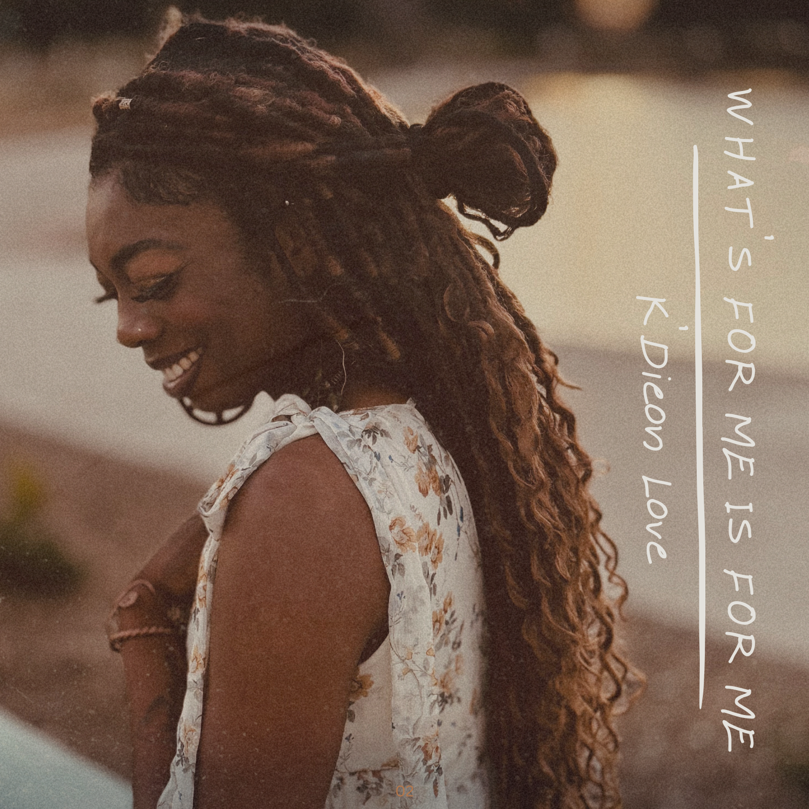 Side profile of a smiling woman with long, curly dreadlocks wearing a floral dress outdoors at sunset.