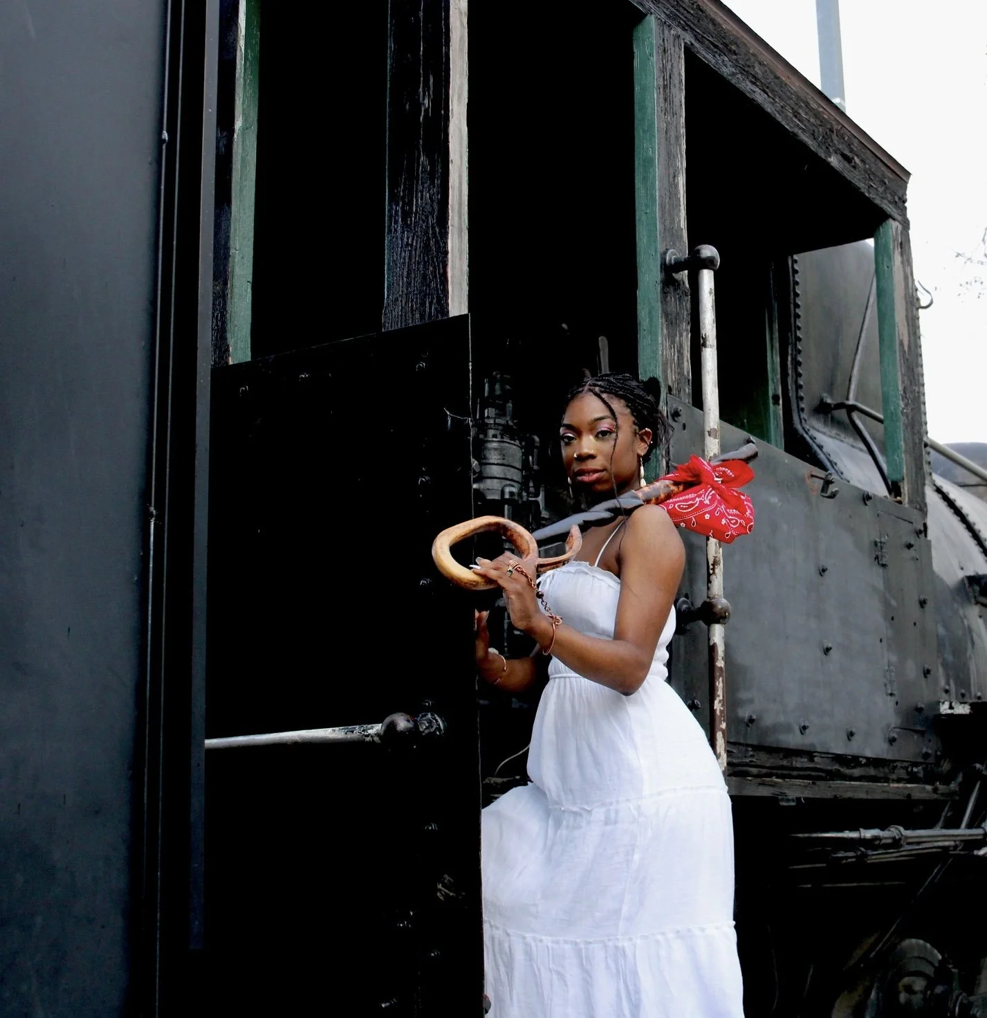 A woman in a white dress holding a vintage cane stands next to a black steam locomotive.