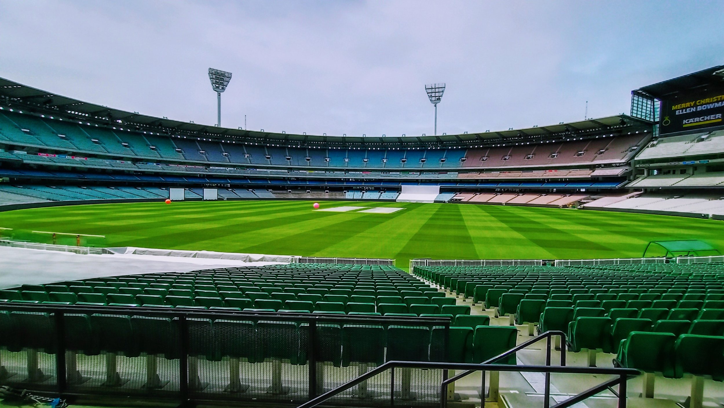Empty cricket stadium with green field and colorful seats, view from stands.