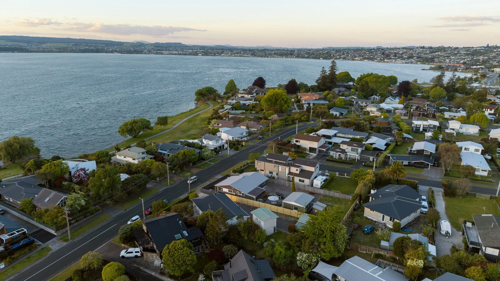 Aerial view of a residential neighborhood with many houses, trees, and streets near a large body of water.