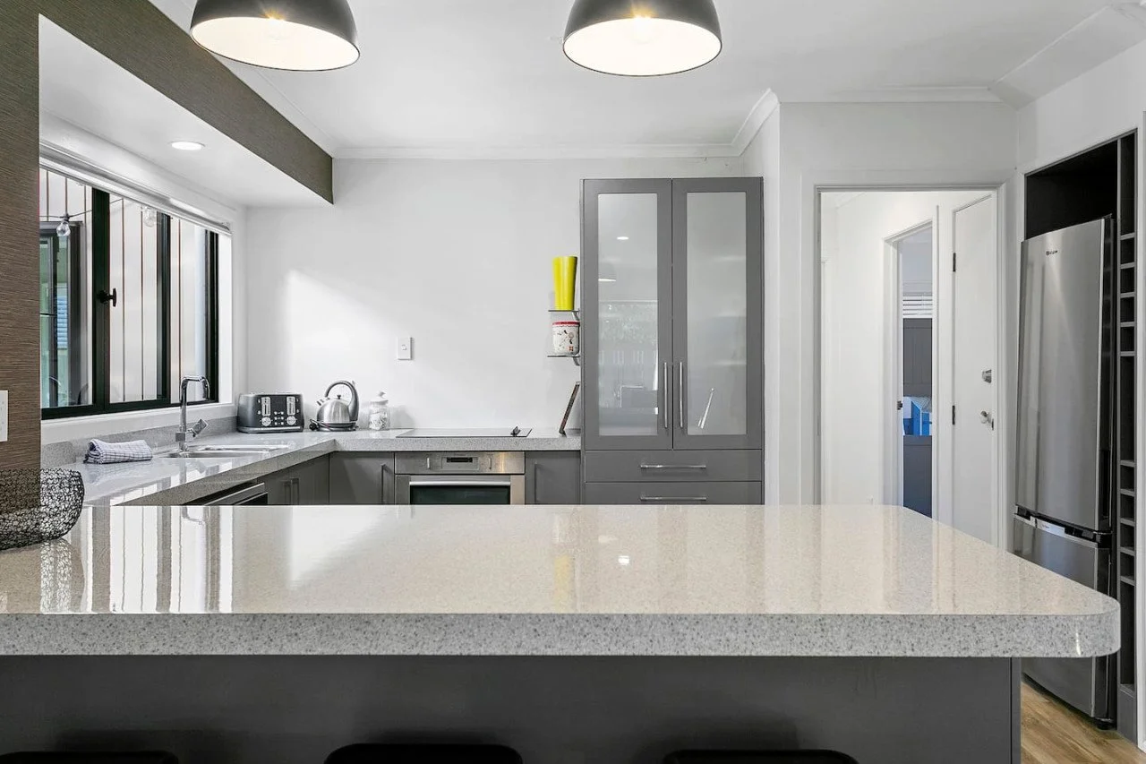 Modern kitchen with gray cabinets, white countertops, a stainless steel refrigerator, and a large window letting in natural light.