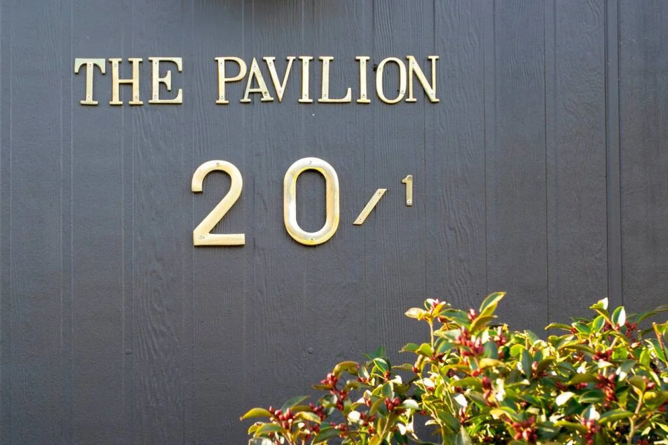 Sign reading 'The Pavilion 201' with a bush of green leaves and red berries in the foreground.