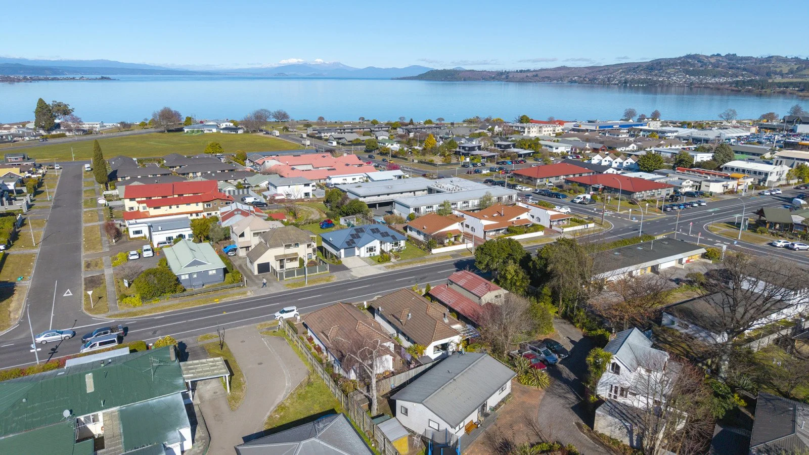 An aerial view of a residential neighborhood near a large body of water, showing houses, roads, and some trees, with mountains in the background.