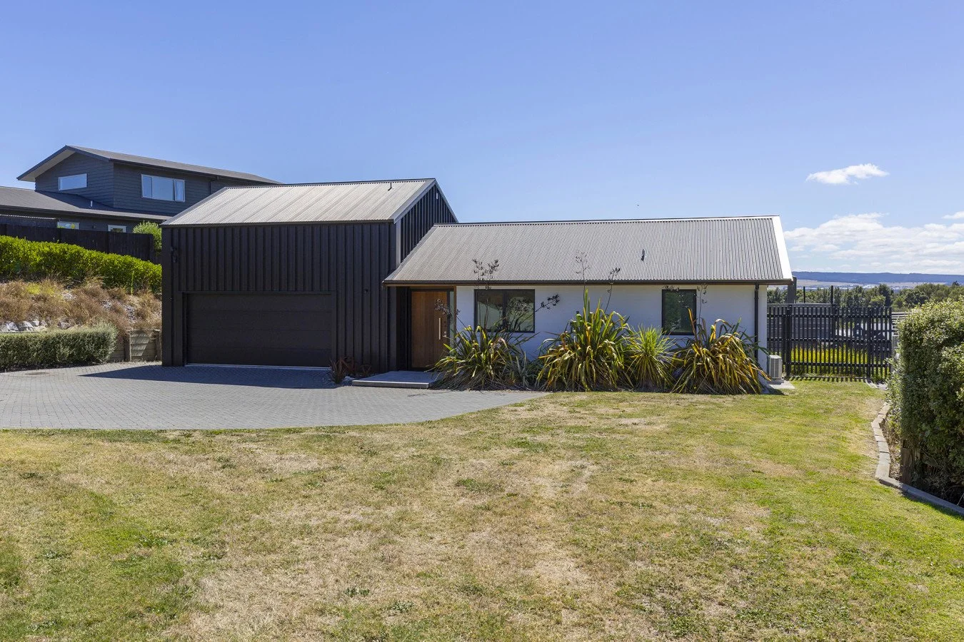 Modern house with black and white exterior, metal roof, and landscaped yard under a clear blue sky.
