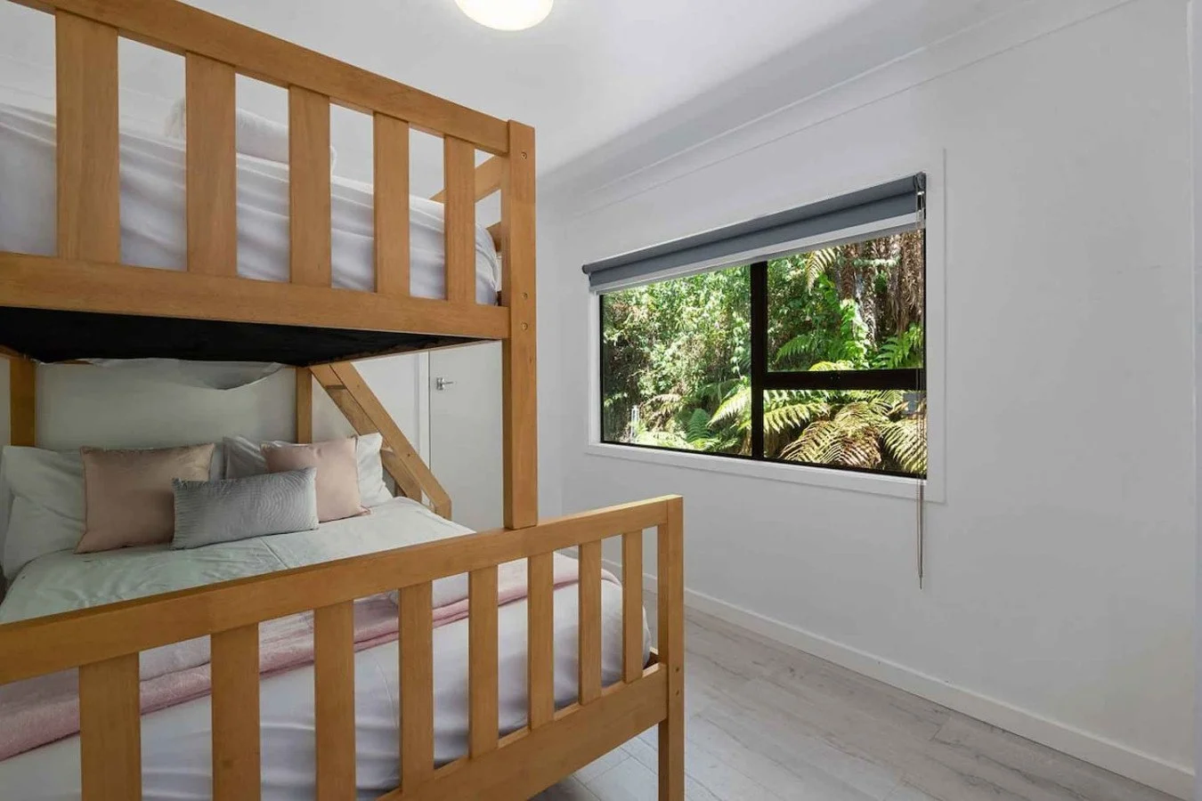 Bedroom with a wooden bunk bed, a window with a view of green foliage, and a roller shade.