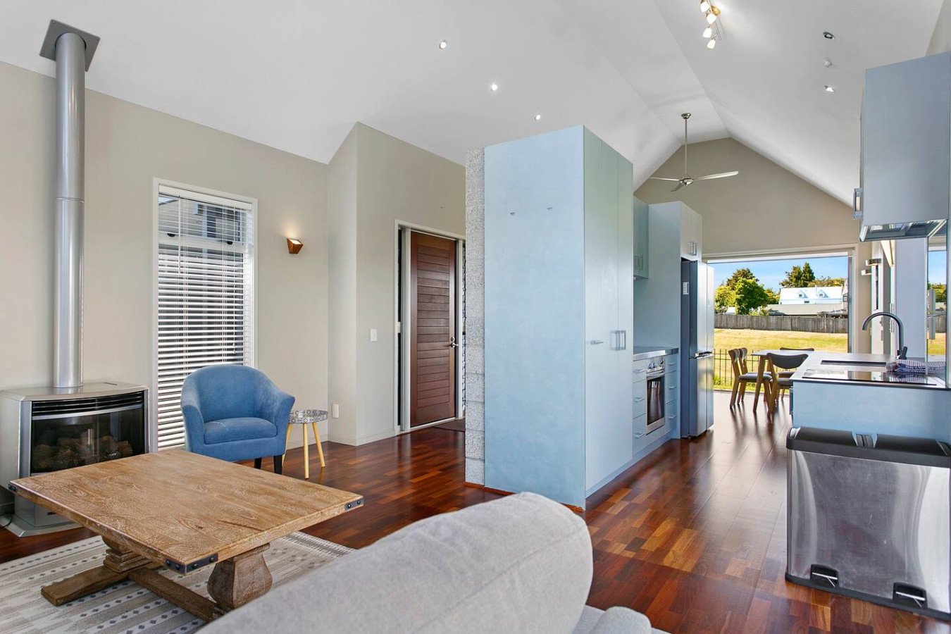 Open-concept living room and kitchen with hardwood floors, blue accent walls, and large windows showing outdoor scenery.