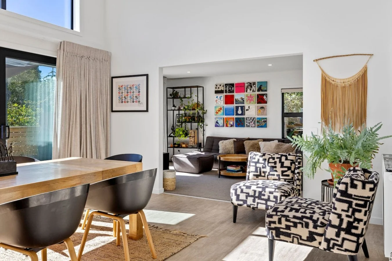 Modern dining and living room with natural light, patterned chairs, artwork, and indoor plants.