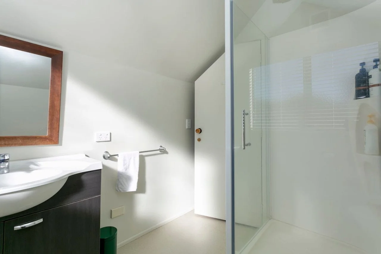A bathroom with a white sink, mirror, towel rack, and a glass shower enclosure.