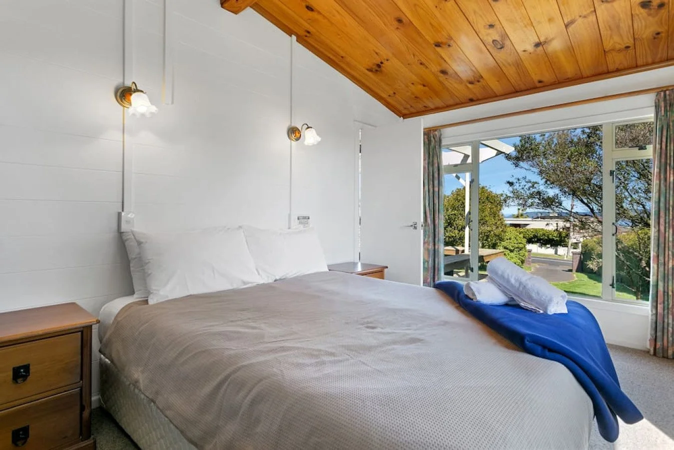 Hotel room with a bed, nightstands, and large window showing trees outside.