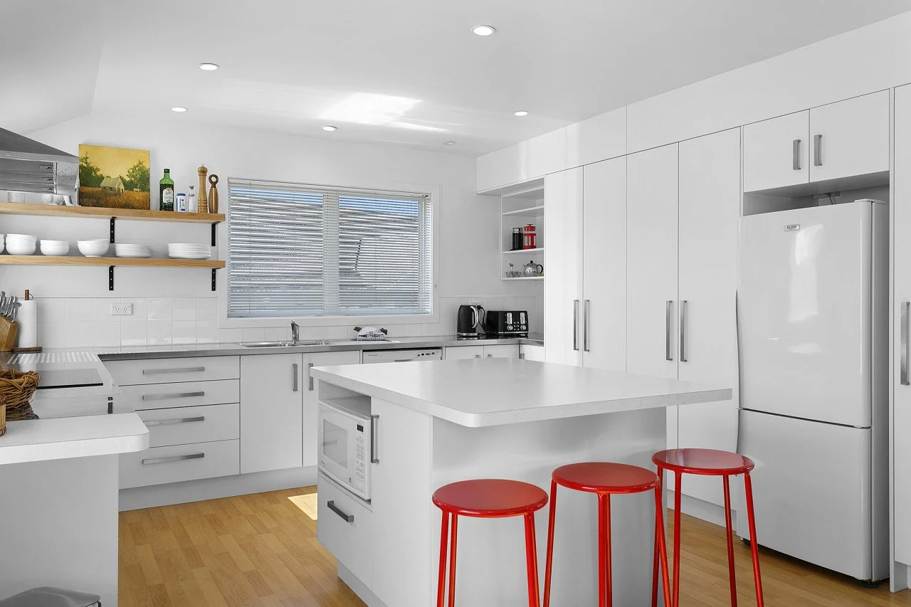 Modern kitchen with white cabinets, a white island with three red stools, and wooden flooring.