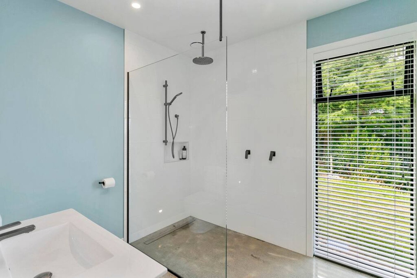 Modern bathroom with a walk-in shower, a window with blinds, and a light blue accent wall.